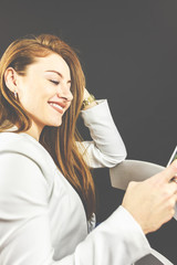 Junge Frau mit Jeans und weißem Blazer lächelt und hält Ihr Smartphone in der Hand, telefoniert und liest Nachrichten. 