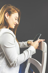 Junge Frau mit Jeans und weißem Blazer lächelt und hält Ihr Smartphone in der Hand, telefoniert...