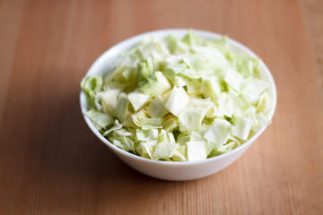 green cabbage sliced in a white plate on a wooden table and light background close-up