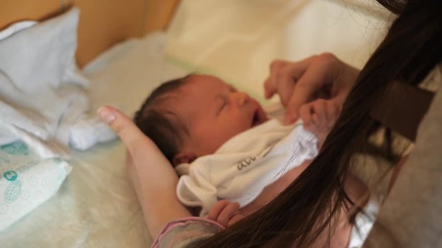 Young mother puts clothes on infant baby child - pants, sweater and bodykit before discharge from maternity hospital