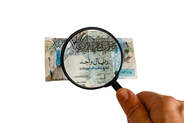 one Qatar Riyal and magnifying glass in hand isolated on white background, obverse front side