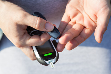 Caucasian man using lancelet on finger, close up view of human hands with glucometer