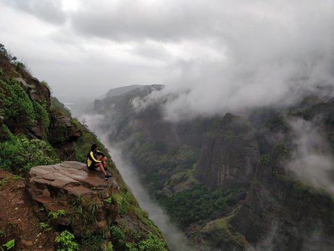 person sitting on rock on top of mountain with fog