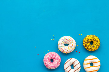 Glazed decorated donuts for sweet break on blue background flat lay copy space