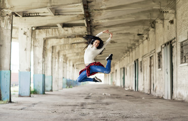 Street dancer. Young woman jumping high on industrial background on sunny day. 