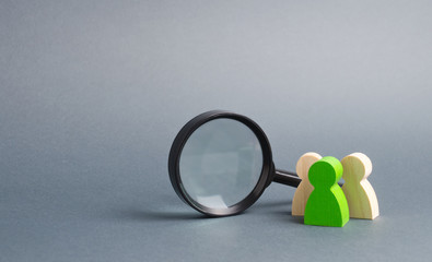 Three wooden human figure stands near a magnifying glass on a gray background. Human resources,...
