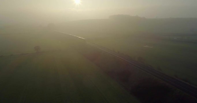 Moody misty morning aerial of train passing through the English countryside on the railway track