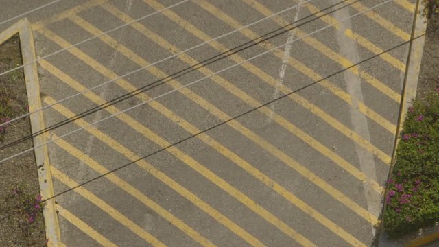 Steady, bird's eye view, medium close up shot of telephone wires and a parking lot with painted lines indicating no parking is allowed.