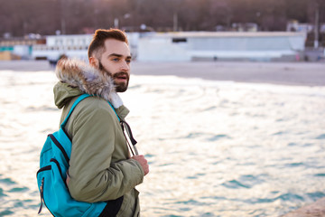 Stylish young man with backpack near sea