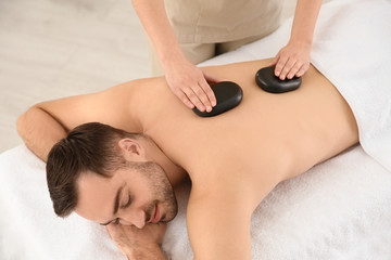 Obraz na płótnie Canvas Handsome man receiving hot stone massage in spa salon, above view