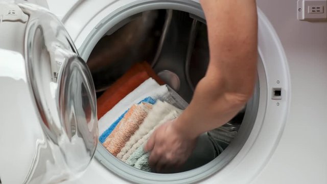 woman puts a stack of laundry in the washing machine and closes the door. Closeup.