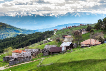 Fototapeta premium Cloudy spring day over highest village on Balkans and Bulgaria - Ortsevo in Rhodope mountain. High snowy Pirin mountain at background.