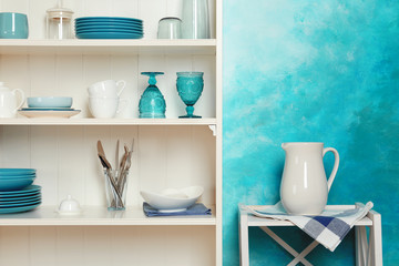 White shelving unit with set of dishware near color wall