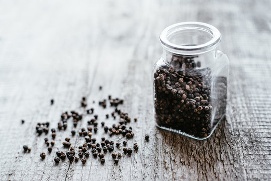 Black pepper is poured from a glass jar on a wooden surface