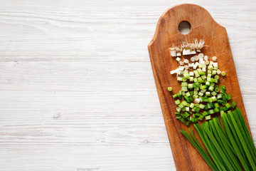 Chopped green onions on a rustic wooden board over white wooden background, top view. Overhead, flat lay, from above. Copy space.