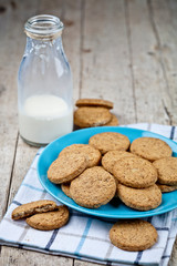 Fresh baked oat cookies on blue ceramic plate on linen napkin and bottle of milk on rustic wooden table.