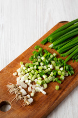 Chopped green onions on a rustic wooden board over white wooden background, low angle view. Close-up.