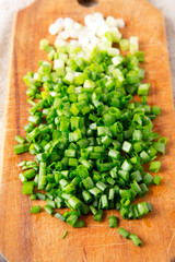 Chopped green onions on a rustic wooden board, side view. Close-up.