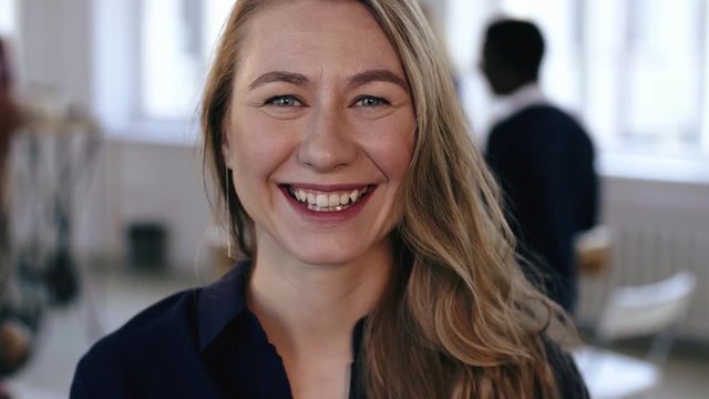 Close-up portrait of happy Caucasian blonde business woman posing at trendy modern office workplace, smiling cheerfully.