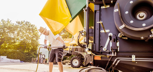 The mechanics repair the yellow and green combine harvester in the farm yard. 