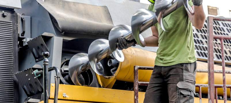 The mechanics repair the yellow and green combine harvester in the farm yard. 