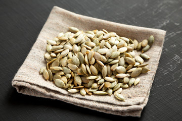 Roasted pumpkin seeds on a black wooden surface, side view. Close-up.