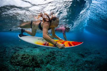 Two young surfers man and woman dive with their surfboards under the breaking ocean wave