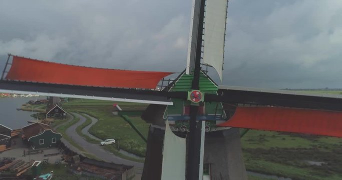 Aerial pulling out from spinning colourful blades of traditional historic Dutch windmill in Zaanse Schans North Holland Nederland Netherlands sustainable clean energy tourist attraction to reveal riverside context and other windmills