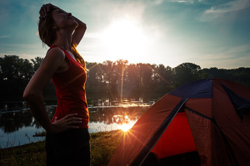 Fototapeta na wymiar Young woman hiker stands near the tent and enjoys sunrise
