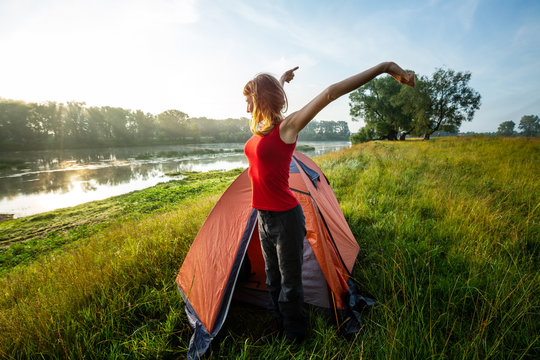 Young woman hiker stretches near the tent and greets the sun