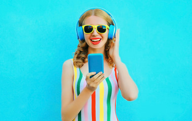 Portrait happy smiling woman holding phone listening to music in wireless headphones on colorful blue background