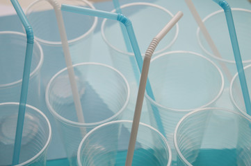 Plastic cups with white and blue straw tubules. Concept of plastic things in everyday life. Selective focus, top view.