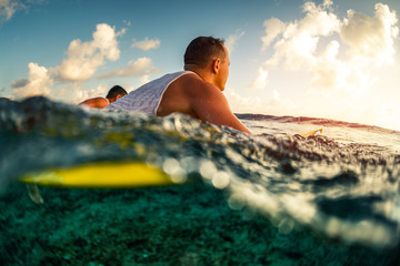 Surfers paddle in the ocean at sunset