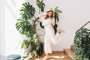Funny young lady in trendy pants standing on one leg and showing peace sign with smile. Laughing...