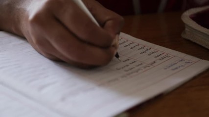 Handheld, close up shot of a hand writing in a notebook. The hand then turns a page.