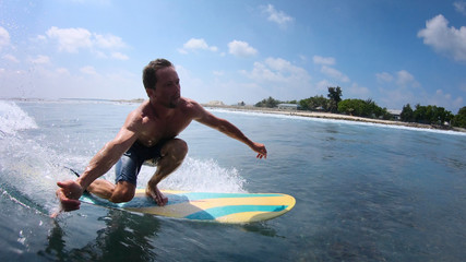 Young man rides the tropical ocean wave on fun board and shows the Shaka sign