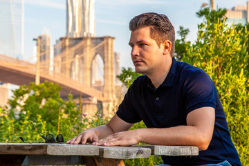 Male model sitting at the table near a Brooklyn Bridge