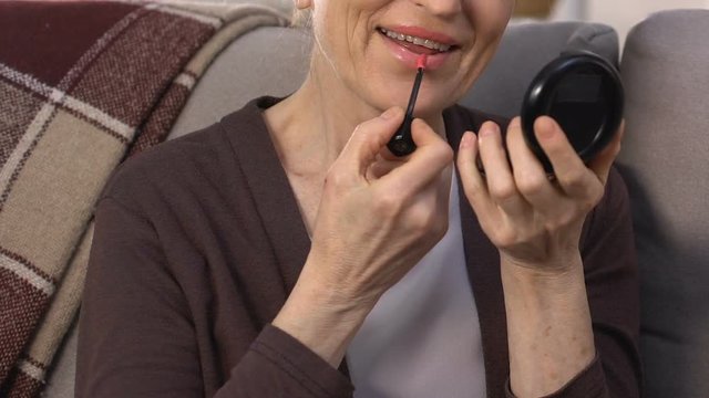 Senior woman painting lips with red lipstick, preparing for romantic date