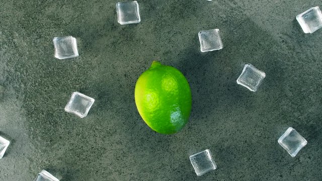 Macro shot of fresh green lime rotating on dark surface with crystal ice cubes. 4K close up footage.