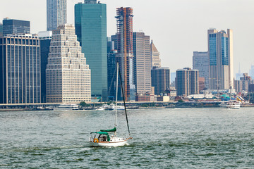 View of midtown Manhattan skyline and sailboat that is cruising on East River during sunny summer day in New York City, USA