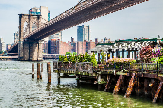 Amazing panorama view of New York city skyline and Brooklyn bridge with restaurant, skyscrapers and East River flowing during daytime in United States of America