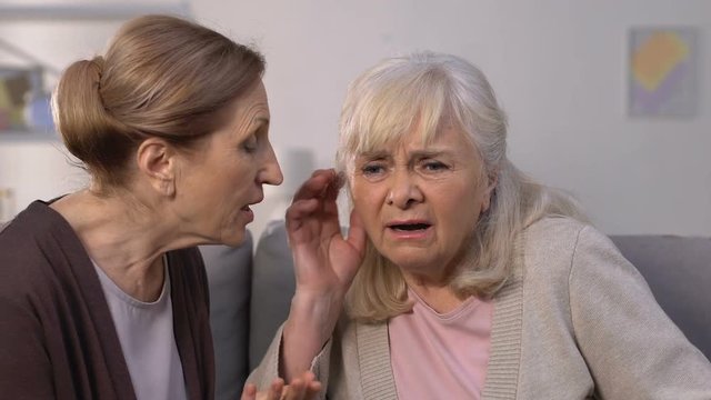 Aged woman shouting to friend suffering from hearing loss disease, deafness
