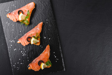 Appetizer bruschetta with fillet salmon, olives and lemon on ciabatta bread on stone slate background. Healthy food concept
