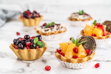 Fruit tart with orange, pomegranate, currant and cream, cakes and sweetness on light marble background. Delicious dessert and candy bar