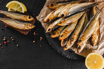 Smoked fishes sprat marinated with spices, salt, greens and slice of bread on plate over dark stone...