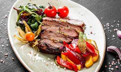 Grilled veal steak with salad and vegetables in plate on dark stone background. Hot Meat Dishes, top view.