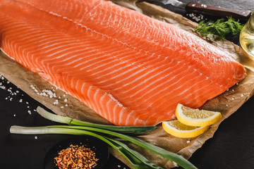 Fresh fillet salmon, red fish steak with spices and lemon on craft paper over dark stone background. Seafood, top view.