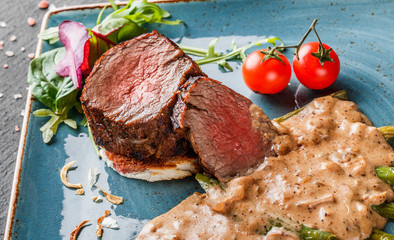 Juicy medium beef fillet steaks mignon with asparagus and mushroom sauce on on dark stone background. Hot Meat Dishes. Top view.
