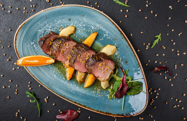 Juicy duck breast steaks with caramelized fruit, mango, apple and sauce of orange on plate over dark stone background. Hot Meat Dishes. Top view.