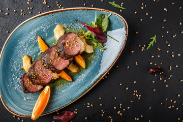 Juicy duck breast steaks with caramelized fruit, mango, apple and sauce of orange on plate over dark stone background. Hot Meat Dishes. Top view.